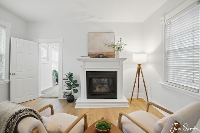 living area featuring baseboards, a glass covered fireplace, and wood finished floors