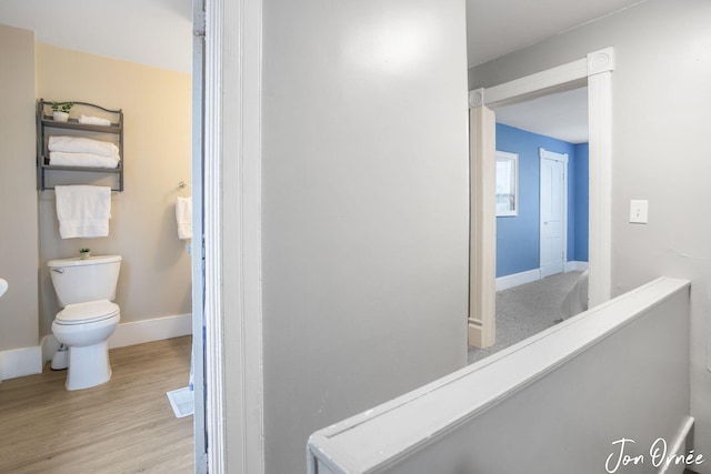 hall with baseboards, an upstairs landing, and wood finished floors