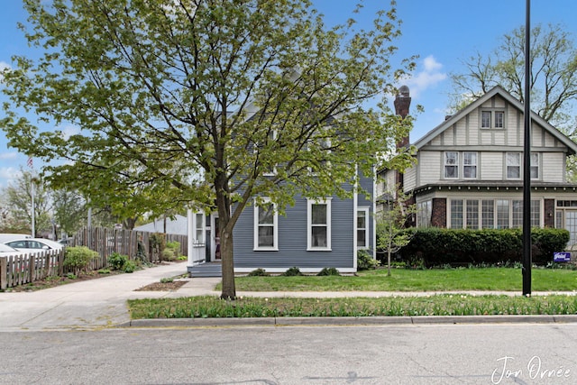 view of front facade featuring brick siding, fence, a chimney, and a front lawn