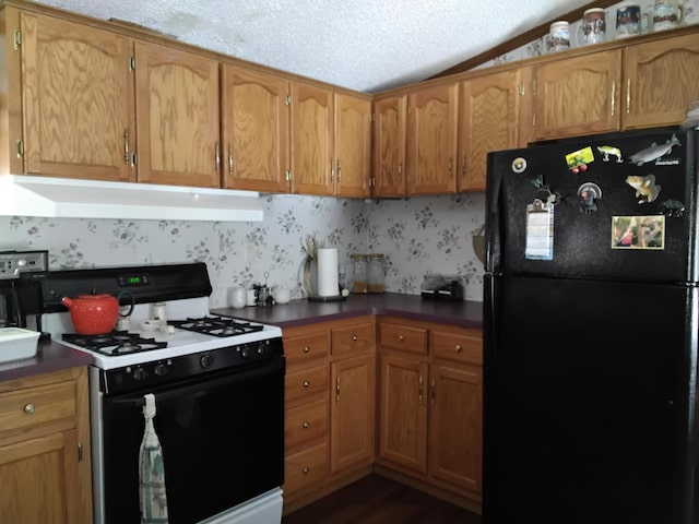 kitchen featuring range with gas stovetop, freestanding refrigerator, under cabinet range hood, and brown cabinetry