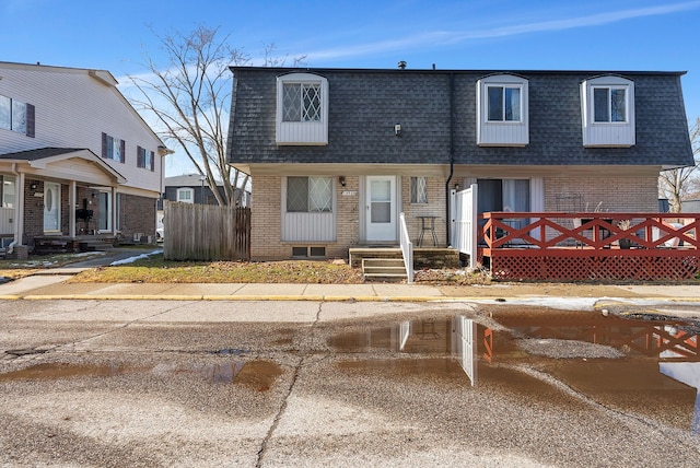 view of front of home with roof with shingles, mansard roof, and brick siding