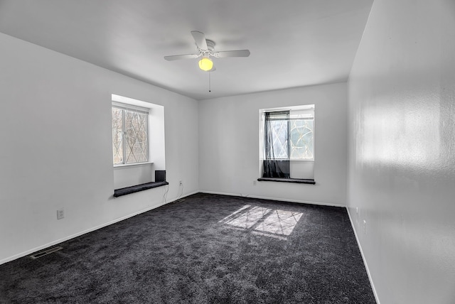 unfurnished room featuring a ceiling fan, visible vents, a healthy amount of sunlight, and dark colored carpet