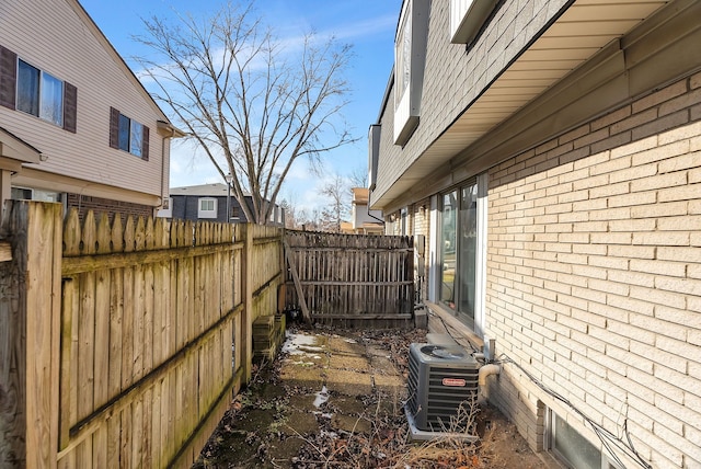 view of property exterior with fence, central AC unit, and brick siding
