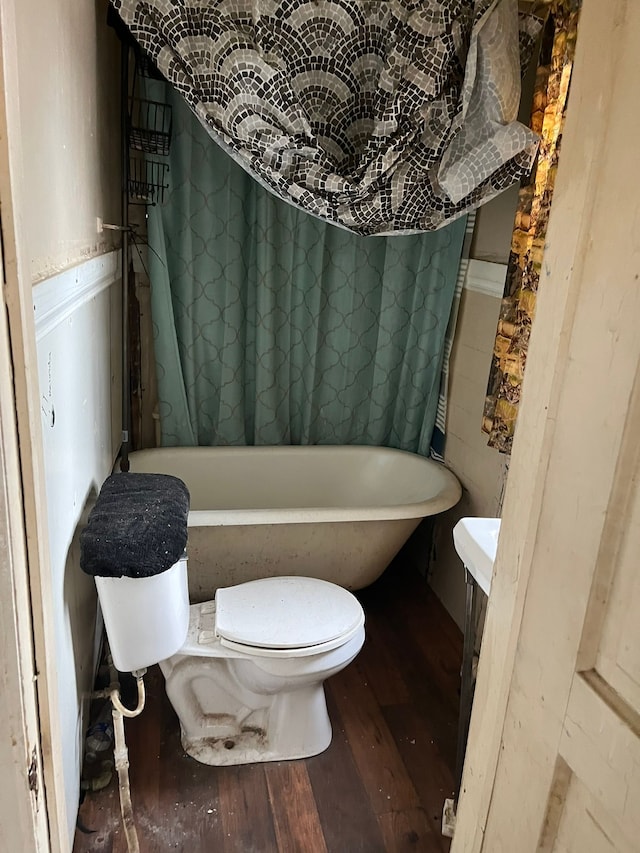 bathroom with toilet, a soaking tub, and hardwood / wood-style floors