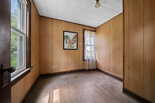 spare room with baseboards, hardwood / wood-style floors, and wood walls