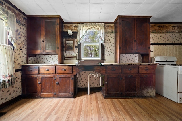 kitchen featuring ornamental molding, light wood finished floors, wallpapered walls, and white gas stove