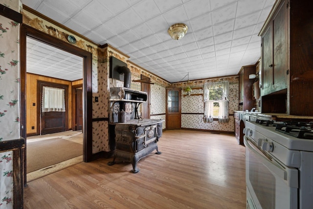kitchen featuring light wood-style flooring, wallpapered walls, open shelves, white gas stove, and a wood stove