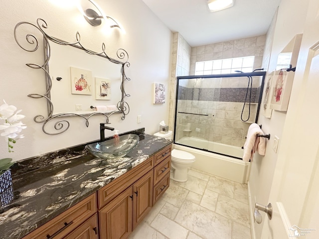 bathroom featuring shower / bath combination with glass door, toilet, stone tile flooring, and vanity