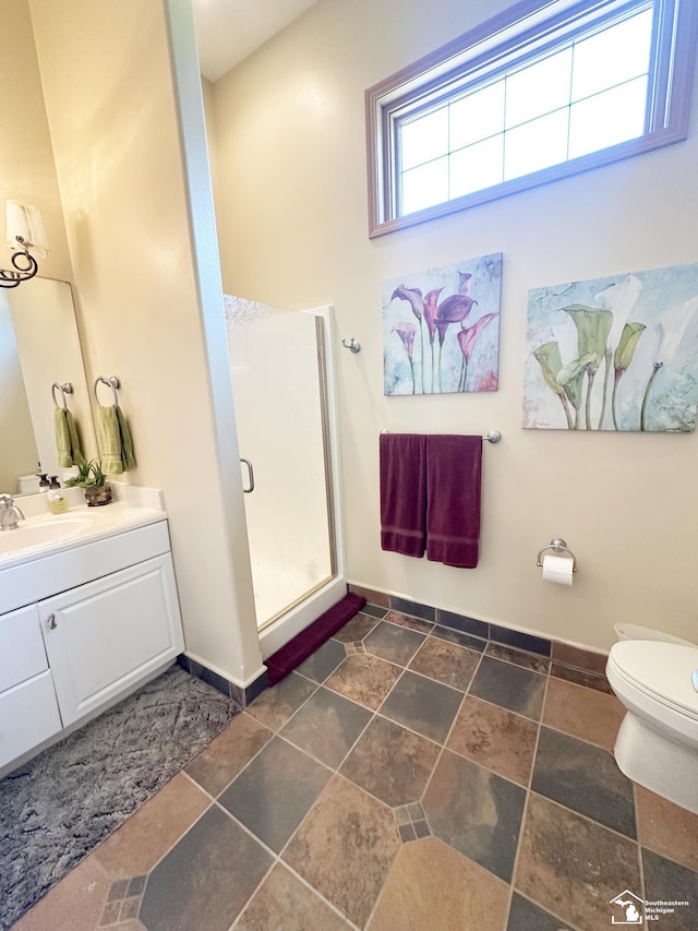bathroom with stone finish floor, a stall shower, vanity, baseboards, and toilet