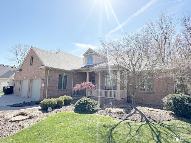 view of front of home featuring a shingled roof, brick siding, a porch, a front yard, and concrete driveway
