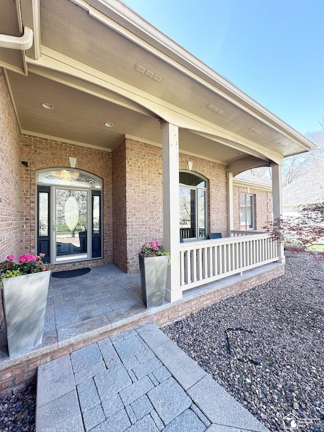 view of exterior entry featuring a porch and brick siding