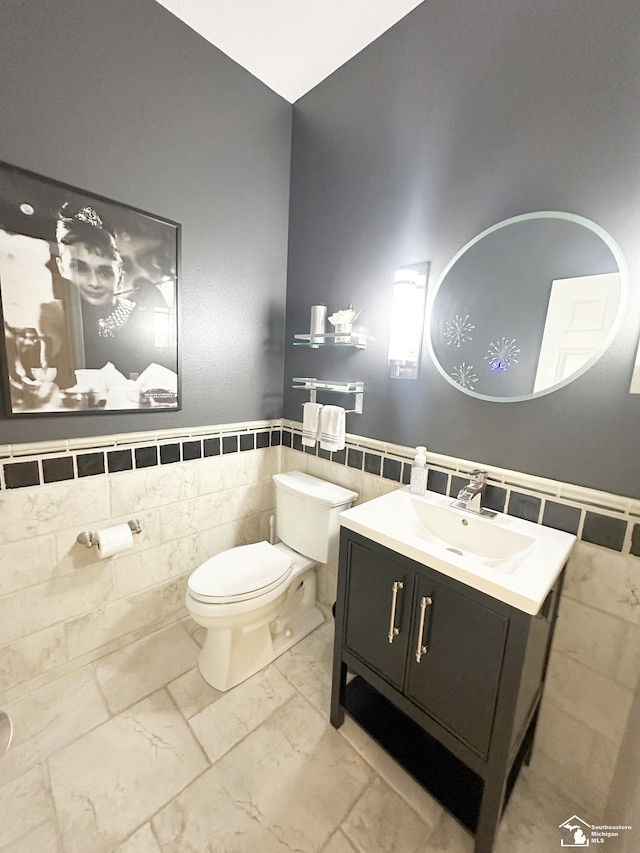 half bathroom with toilet, tile walls, marble finish floor, and a wainscoted wall