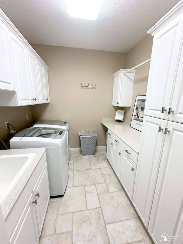 washroom with cabinet space, independent washer and dryer, a textured ceiling, stone tile floors, and baseboards
