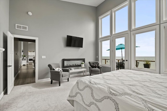 bedroom featuring carpet flooring, a high ceiling, visible vents, and multiple windows