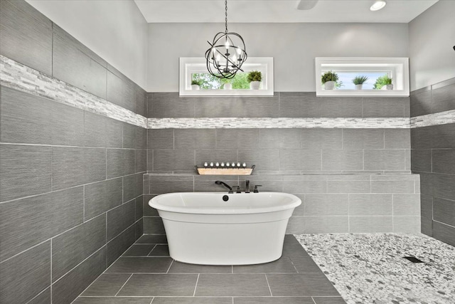 bathroom with a notable chandelier, wainscoting, tile patterned floors, a freestanding tub, and tile walls
