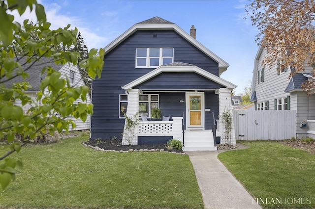 view of front of home with a porch, fence, a chimney, and a front lawn