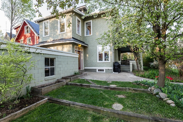 rear view of property with a lawn, a patio, and stucco siding