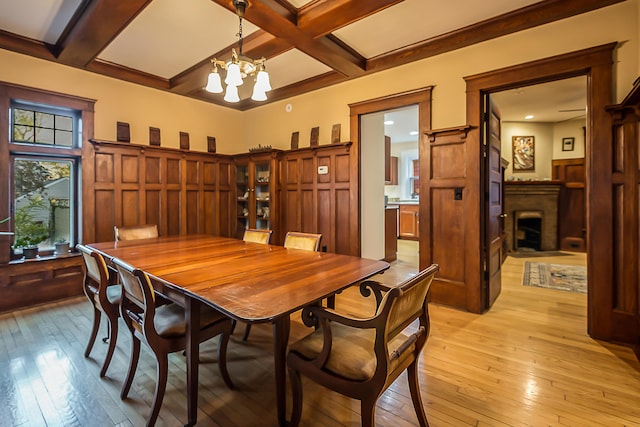 dining room with a fireplace, beam ceiling, an inviting chandelier, coffered ceiling, and light wood-style flooring