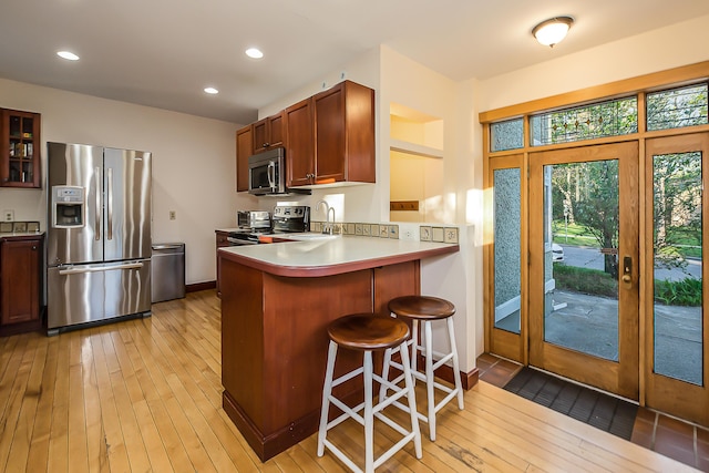 kitchen with glass insert cabinets, appliances with stainless steel finishes, a kitchen breakfast bar, and light wood-type flooring