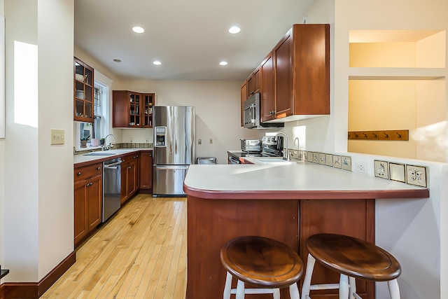 kitchen featuring glass insert cabinets, appliances with stainless steel finishes, a breakfast bar, and a peninsula