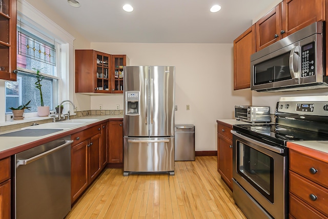 kitchen featuring glass insert cabinets, appliances with stainless steel finishes, light countertops, a toaster, and light wood-style floors