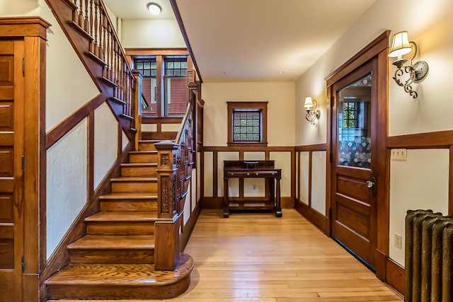 staircase with radiator, wood-type flooring, and a wainscoted wall