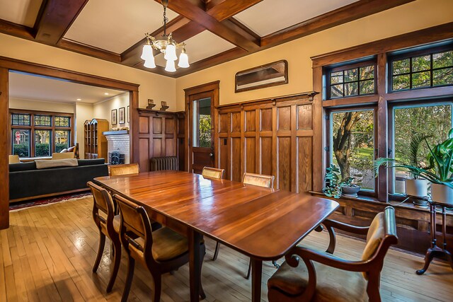 dining space featuring a notable chandelier, beam ceiling, light wood-style floors, a brick fireplace, and coffered ceiling
