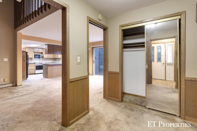 hall with wainscoting, a baseboard heating unit, and light carpet