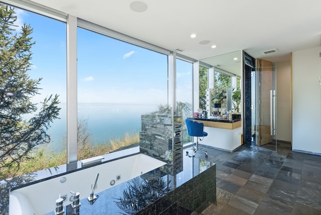 full bath with a wall of windows, stone finish flooring, a tub with jets, a water view, and recessed lighting