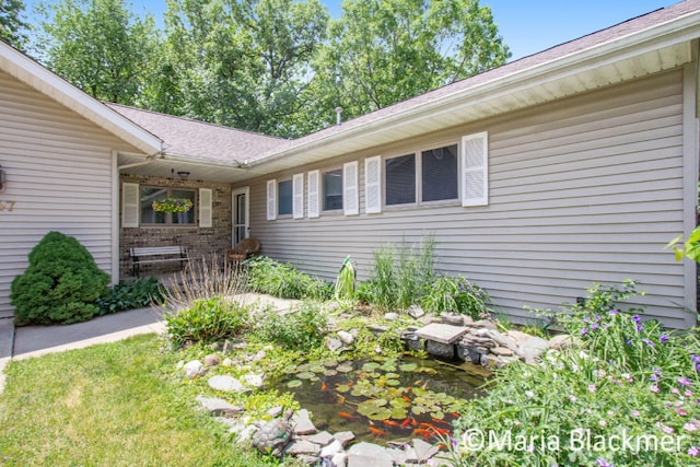 view of exterior entry with brick siding, a small pond, and roof with shingles