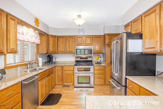 kitchen featuring a sink, brown cabinets, stainless steel appliances, and light wood-type flooring