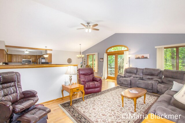 living area with vaulted ceiling, plenty of natural light, ceiling fan with notable chandelier, and light wood-type flooring