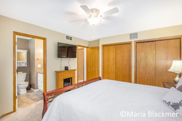 bedroom with visible vents, baseboards, two closets, carpet flooring, and ensuite bath