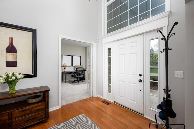 foyer entrance with baseboards, visible vents, wood finished floors, and a towering ceiling