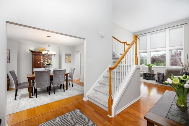 stairway featuring an inviting chandelier, baseboards, a towering ceiling, and wood finished floors