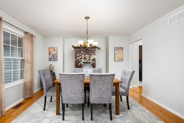 dining room featuring visible vents, light wood finished floors, and a notable chandelier