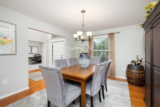 dining area featuring an inviting chandelier, baseboards, and light wood-type flooring