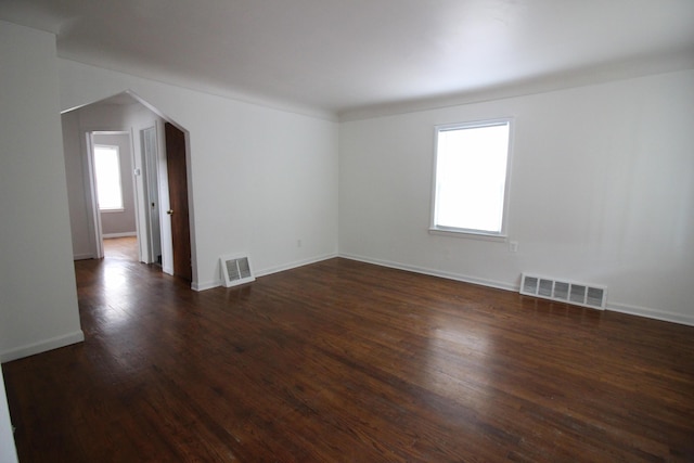 empty room featuring visible vents, arched walkways, baseboards, and dark wood-type flooring