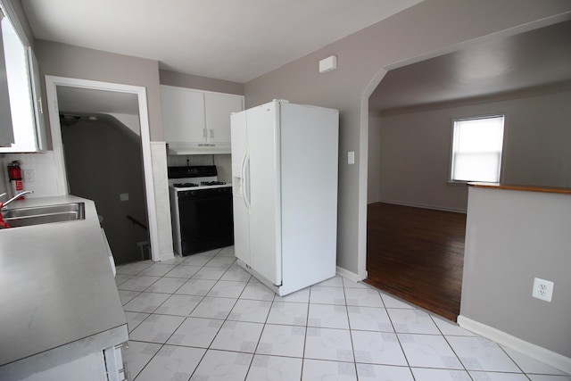 kitchen featuring arched walkways, under cabinet range hood, range with gas cooktop, a sink, and white fridge with ice dispenser