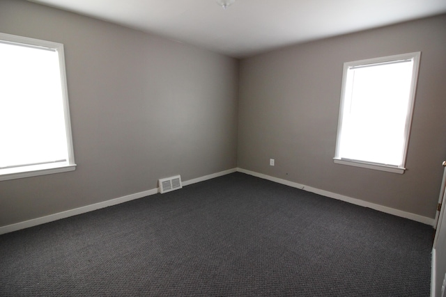 unfurnished room with baseboards, visible vents, and dark carpet
