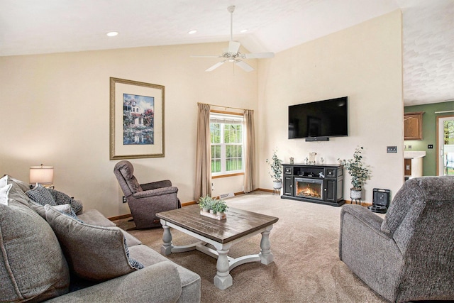 living room featuring a glass covered fireplace, lofted ceiling, light carpet, baseboards, and a ceiling fan