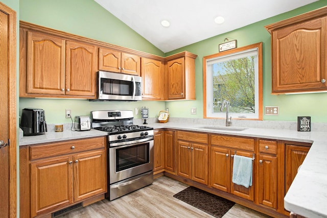 kitchen featuring vaulted ceiling, a sink, light countertops, light wood finished floors, and stainless steel appliances