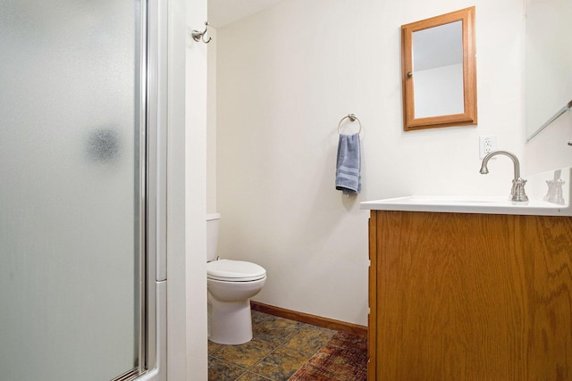 bathroom featuring vanity, toilet, baseboards, stone finish flooring, and a stall shower