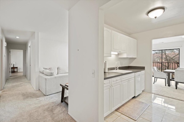 kitchen with dark countertops, light carpet, a sink, dishwasher, and white cabinetry
