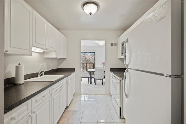 kitchen featuring visible vents, dark countertops, a sink, white appliances, and white cabinetry
