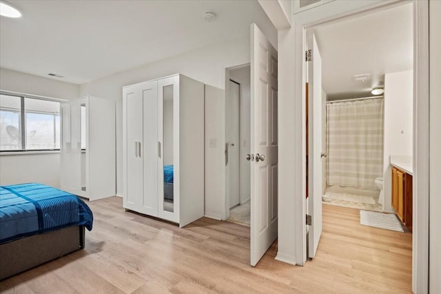 bedroom featuring connected bathroom, visible vents, and light wood-style floors