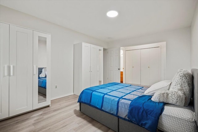 bedroom with baseboards, light wood finished floors, and two closets