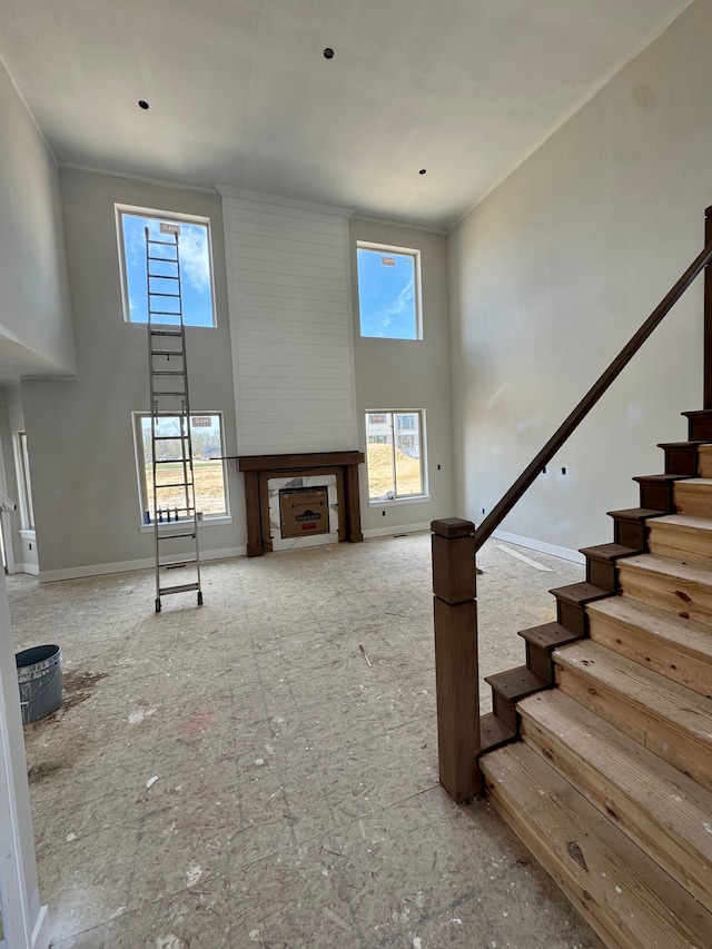 unfurnished living room featuring stairs, a high ceiling, baseboards, and a fireplace