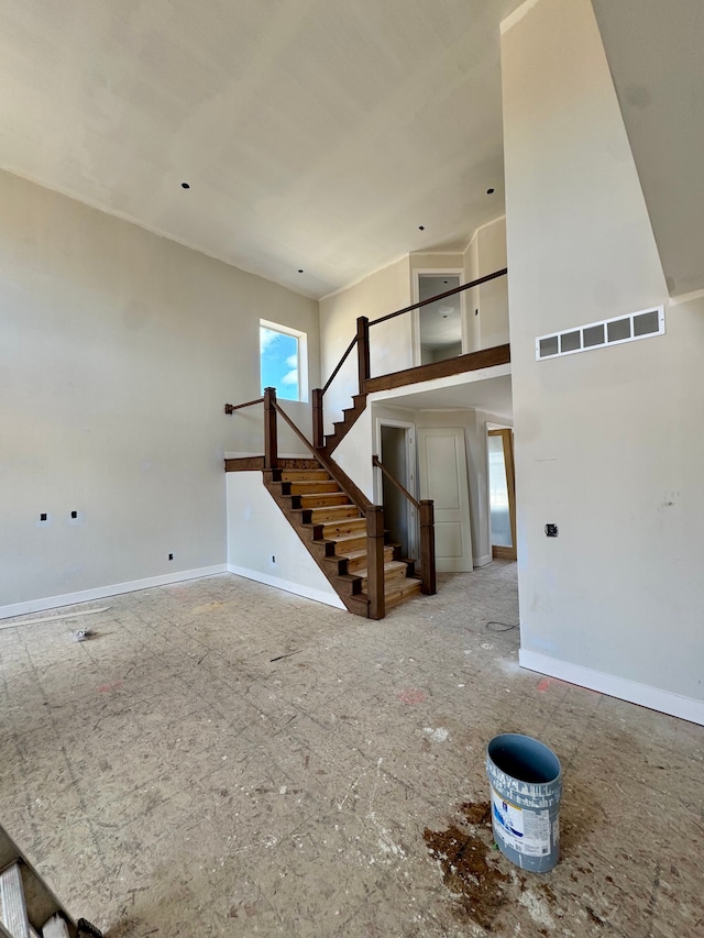 unfurnished living room with baseboards, visible vents, and stairway