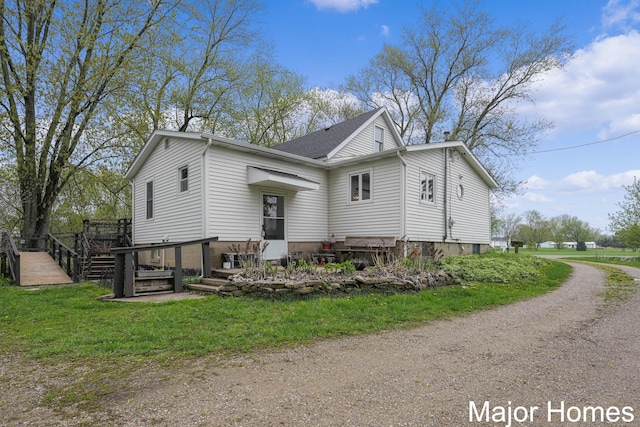 exterior space with a shingled roof, a yard, a wooden deck, and driveway